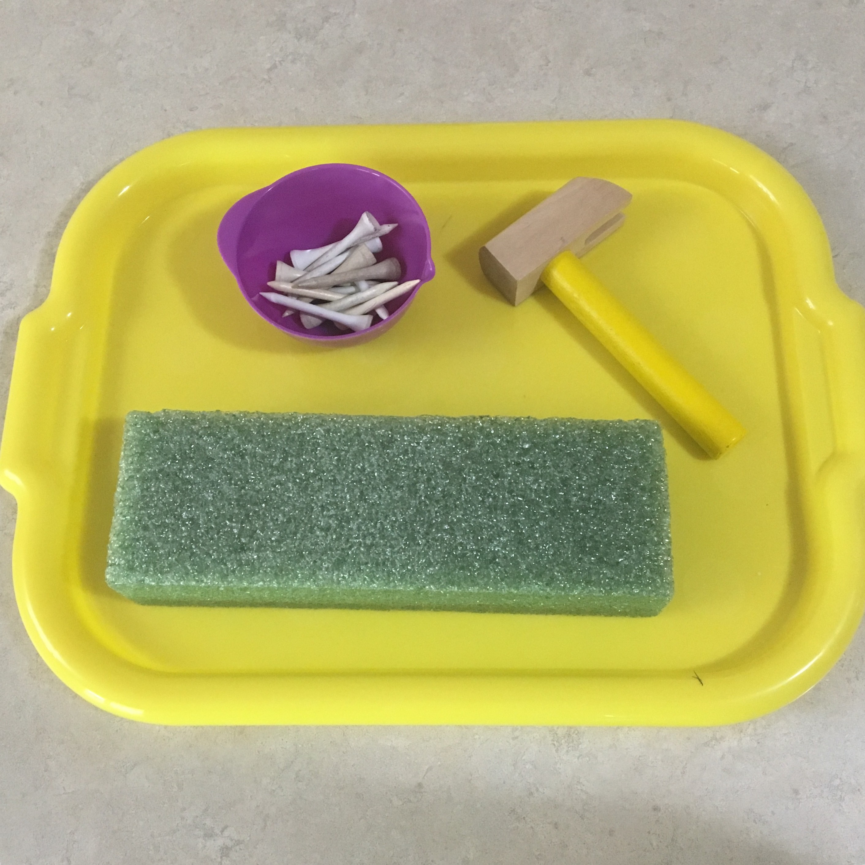 Toddler engrossed in hammering golf tees into a foam block using a toy hammer from a cars tool kit toy