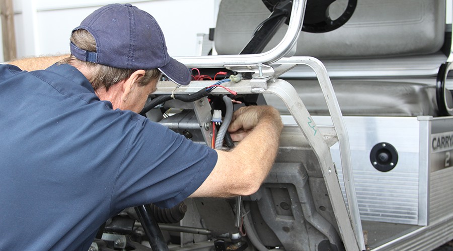 Technician using Club Car service tools for maintenance on a utility vehicle, highlighting Jeffrey Allen Inc.'s expert service.