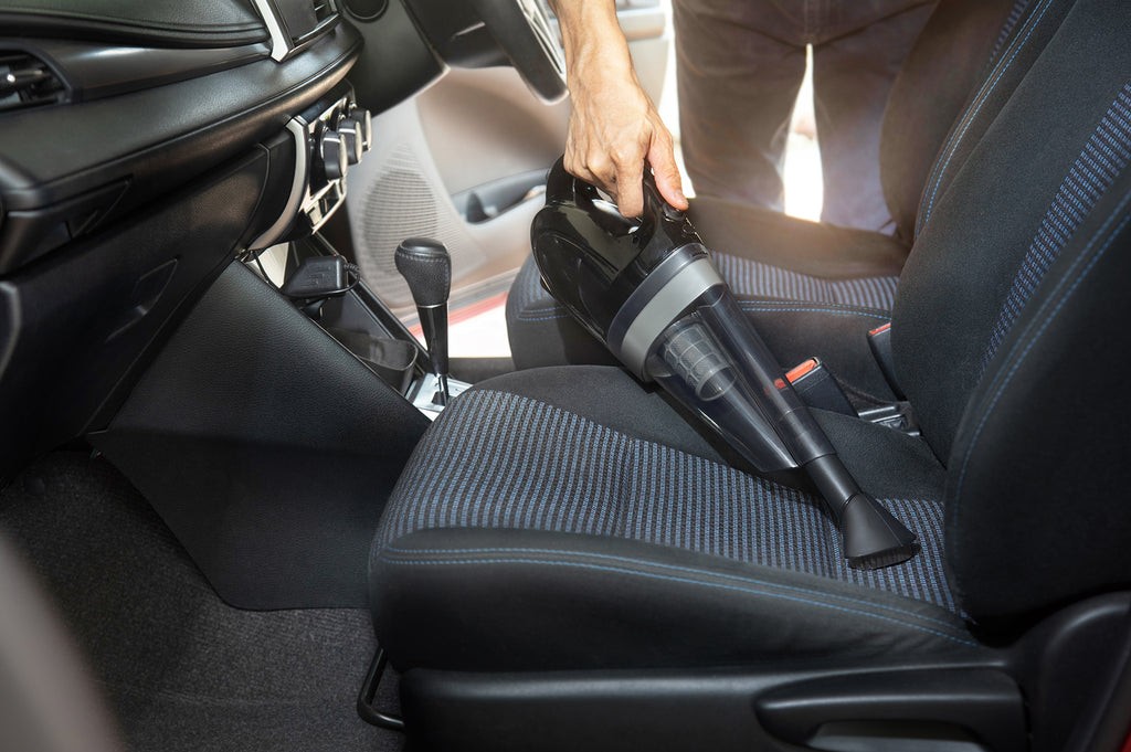 Man Vacuuming a Car interior with hose and brush attachment