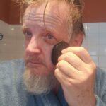 Man using black silicone care face cleaner tool for morning facial cleansing in bathroom.