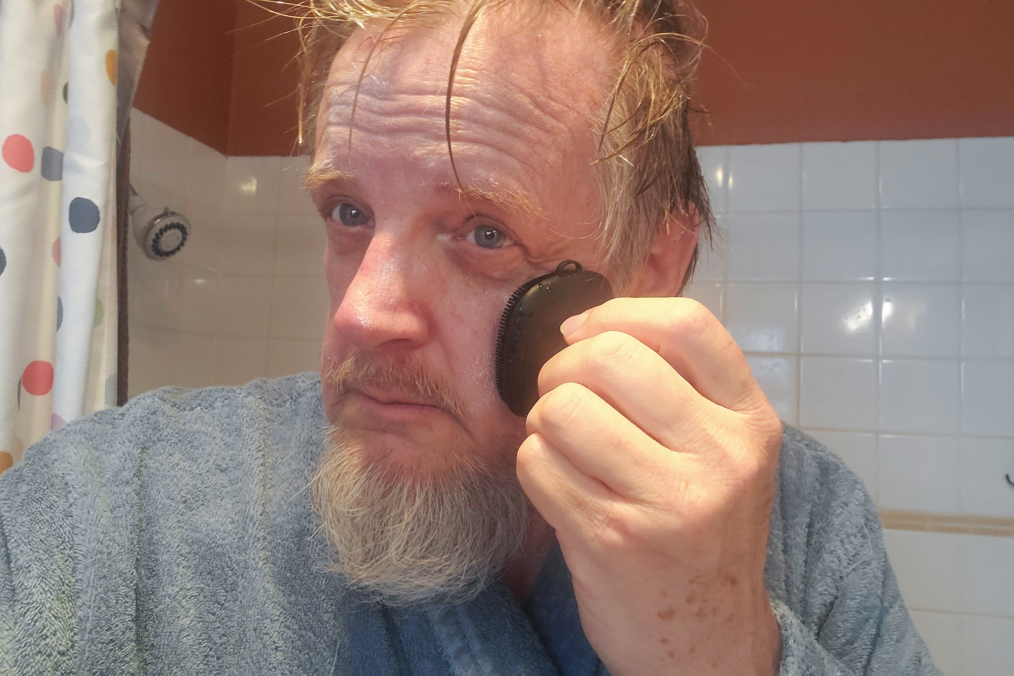 Man using black silicone care face cleaner tool for morning facial cleansing in bathroom.