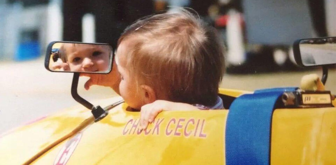 Becca Bertok holding her baby at a race track, showcasing early exposure to motorsports